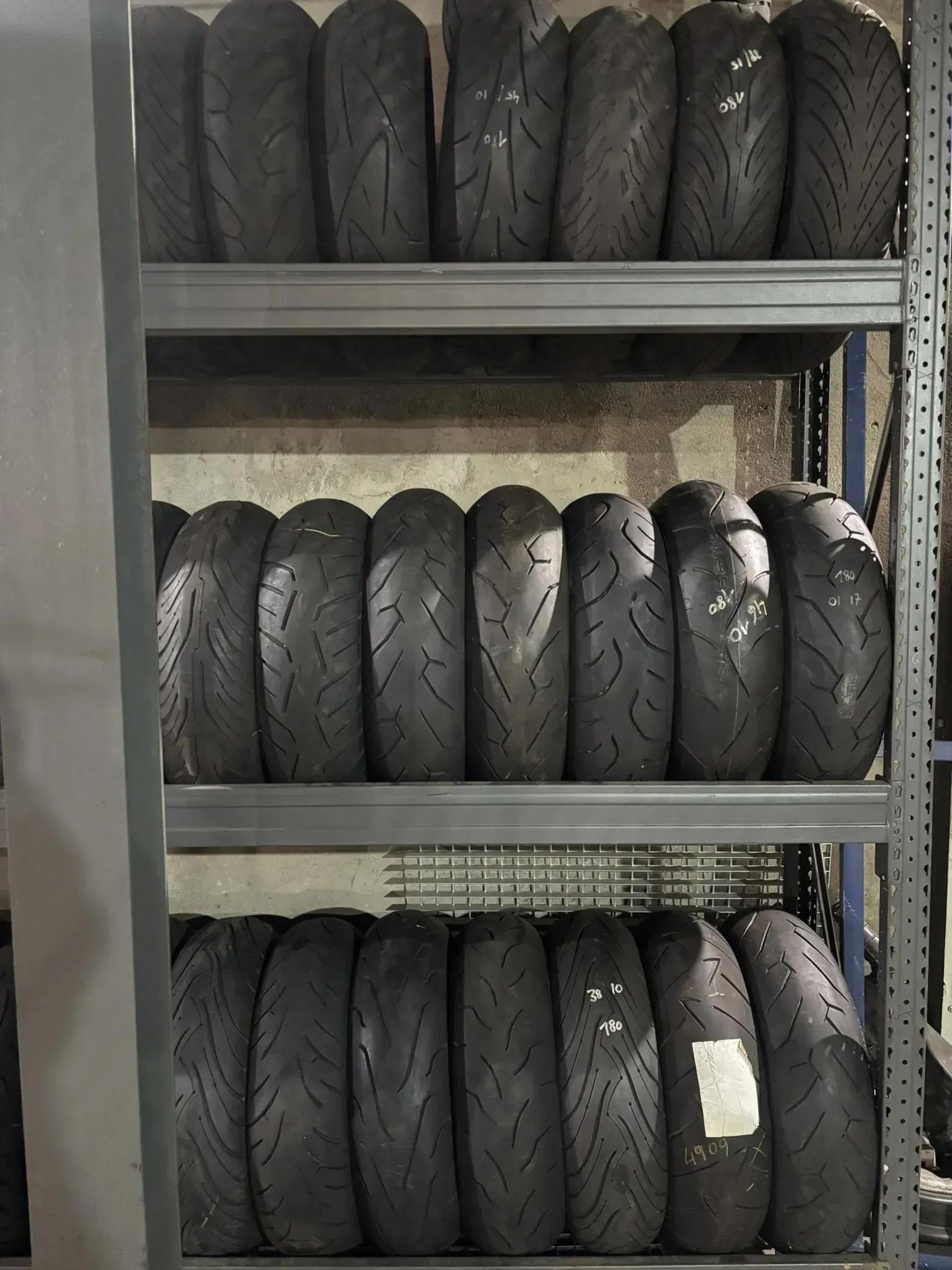 Filas de neumáticos de motocicleta apiladas en estantes de metal en un garaje.