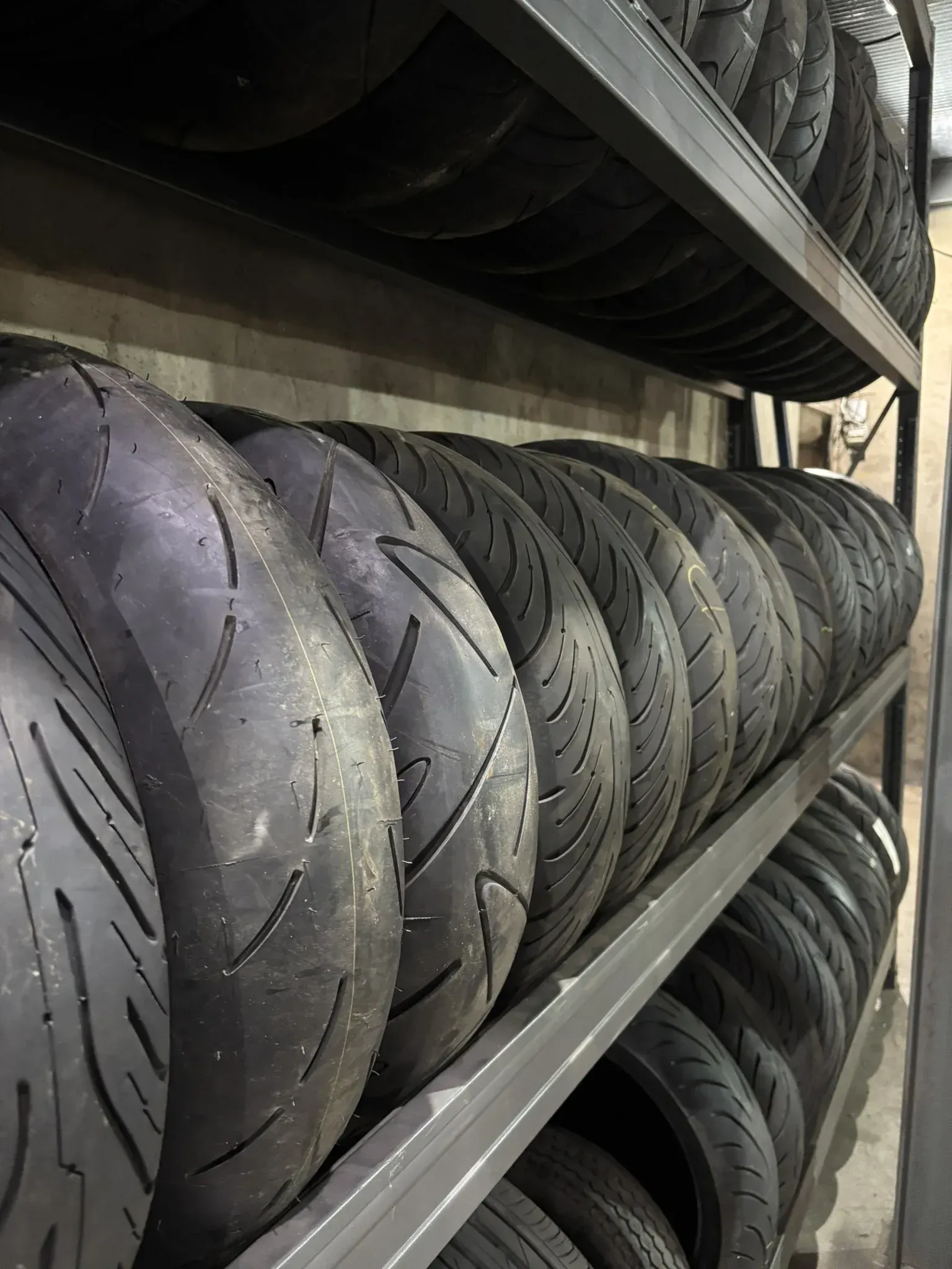 Filas de neumáticos de motocicleta negros apilados en estantes de metal.