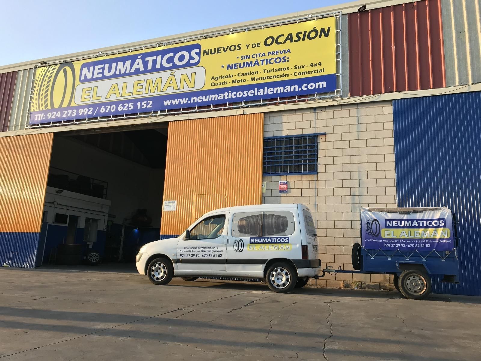 Fachada de una tienda de neumáticos con una camioneta y un remolque estacionados afuera; el letrero dice