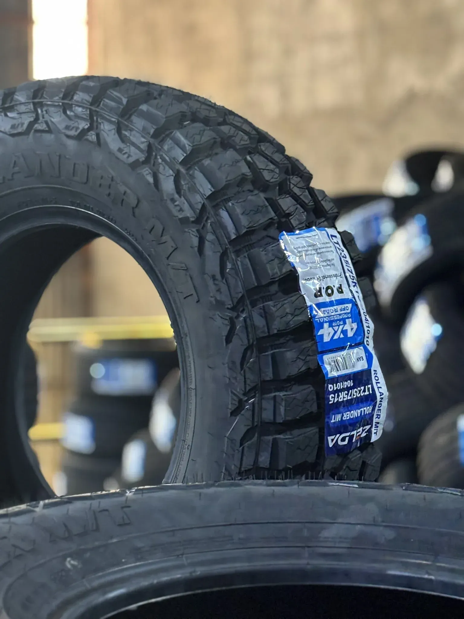 Neumático todoterreno negro con etiqueta, expuesto en una llantera. Otros neumáticos se ven borrosos al fondo.