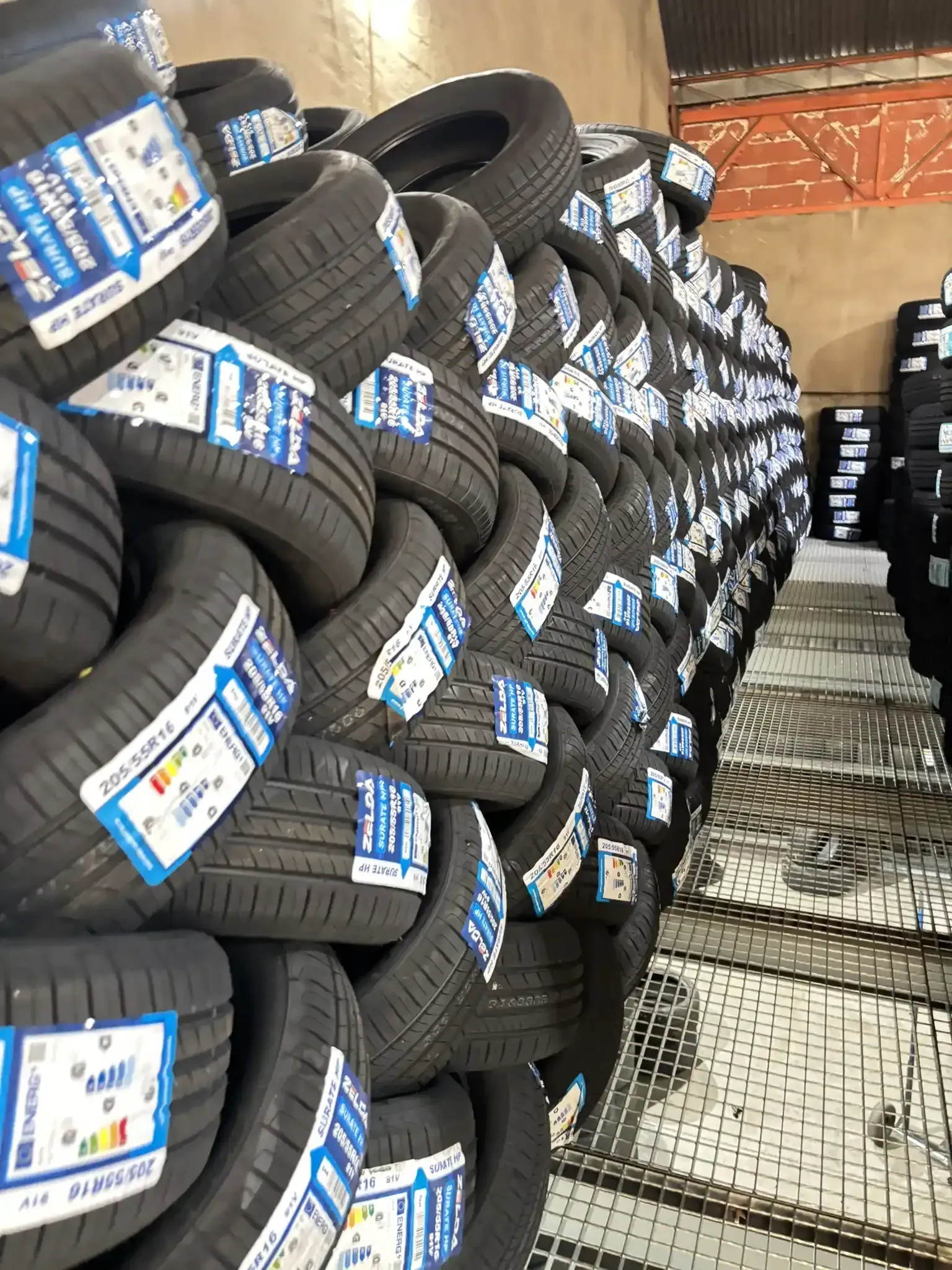 Pilas de neumáticos nuevos dentro de un almacén, con etiquetas visibles.
