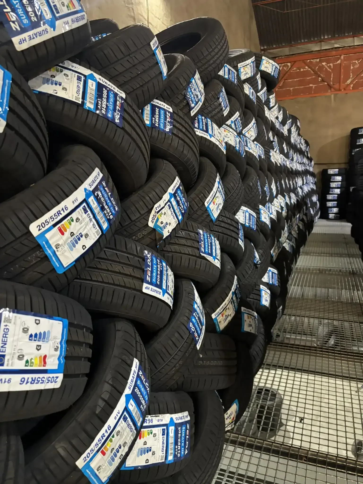 Neumáticos apilados en un almacén, muchos de ellos con etiquetas azules y blancas.