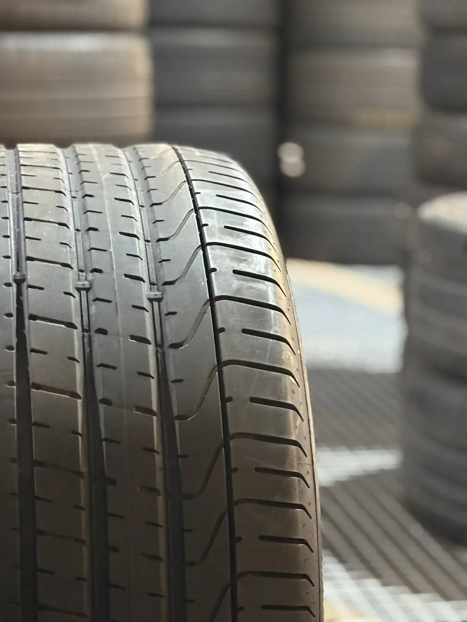 Primer plano de una banda de rodadura de neumático negra con una pila de neumáticos en el fondo.
