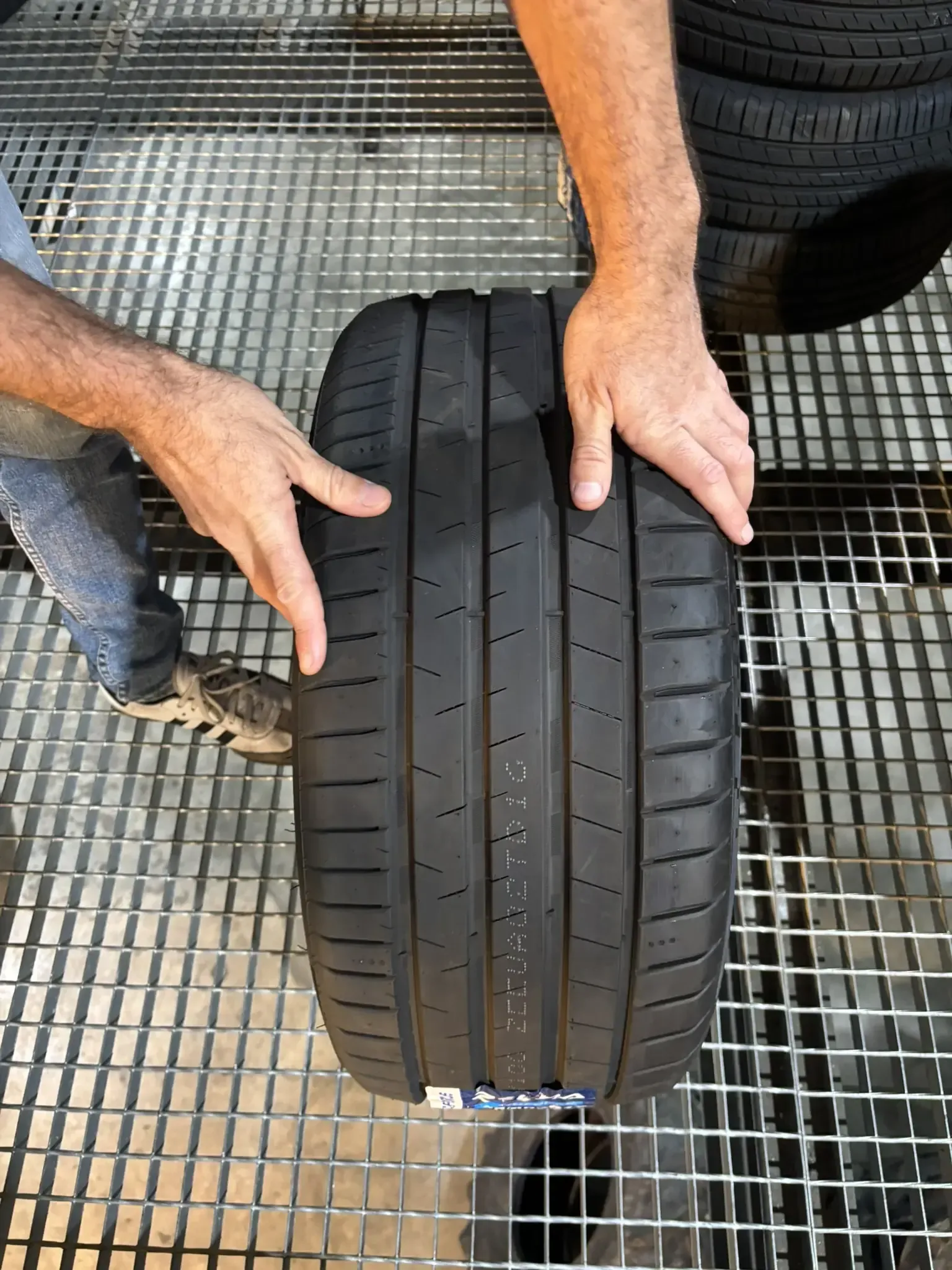 Persona sosteniendo un neumático de automóvil sobre una rejilla metálica.