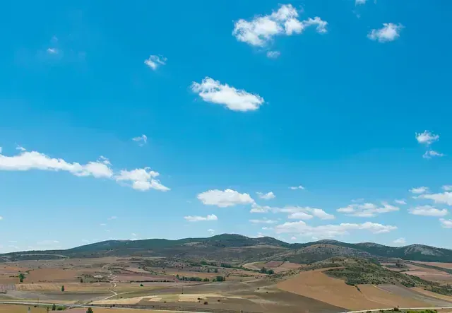 Cielo azul con nubes blancas dispersas sobre colinas marrones onduladas en un paisaje rural.