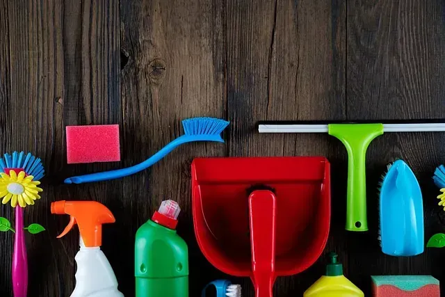Materiales de limpieza sobre una superficie de madera oscura: botellas de spray, cepillos, esponjas, recogedor, escobilla de goma.