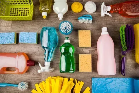 Artículos de limpieza dispuestos sobre una superficie de madera: esponjas, botellas, cepillos para fregar, paños, en varios colores.