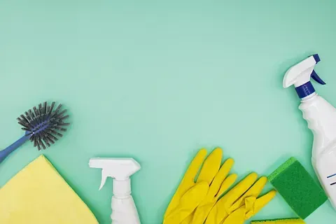 Productos de limpieza sobre un fondo verde menta: cepillo, botellas de spray, esponja, guantes.