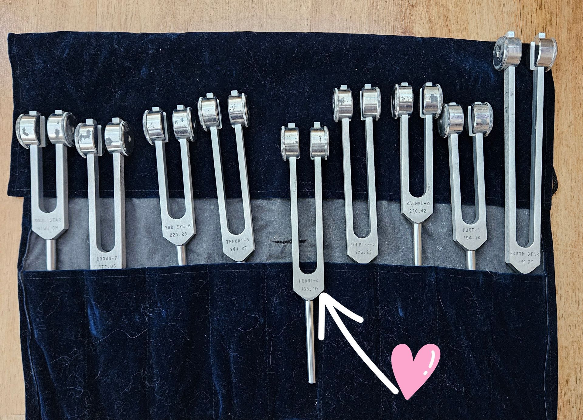 Un juego de diapasones plateados en un estuche de terciopelo azul oscuro, uno marcado con una flecha y un corazón rosa.