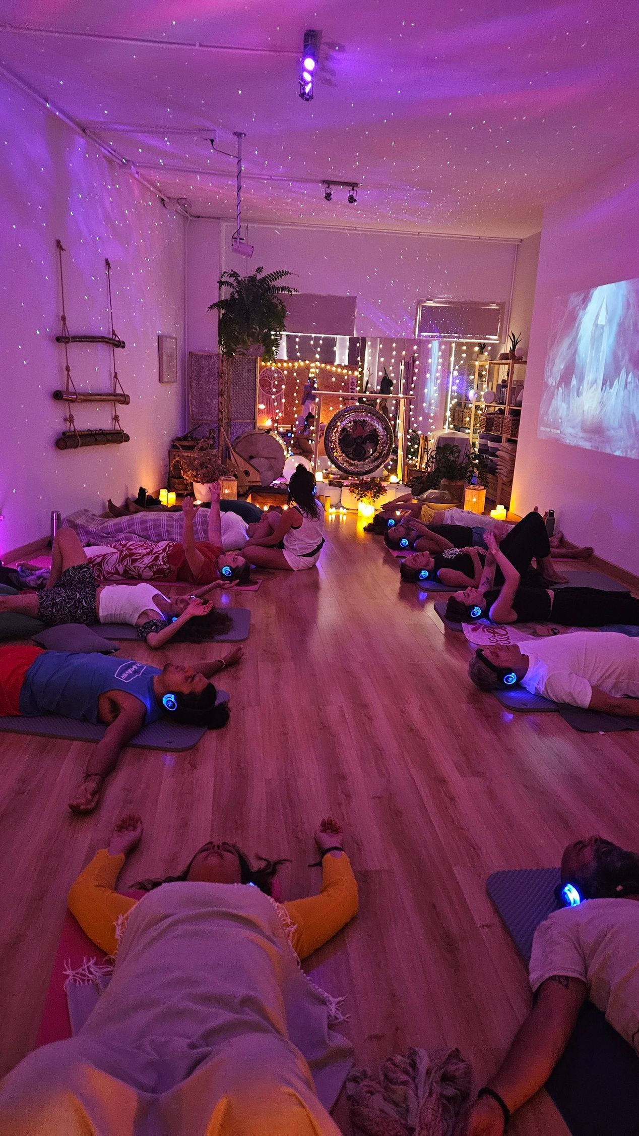 Personas tumbadas sobre colchonetas en una habitación con poca luz, posiblemente un estudio de yoga.