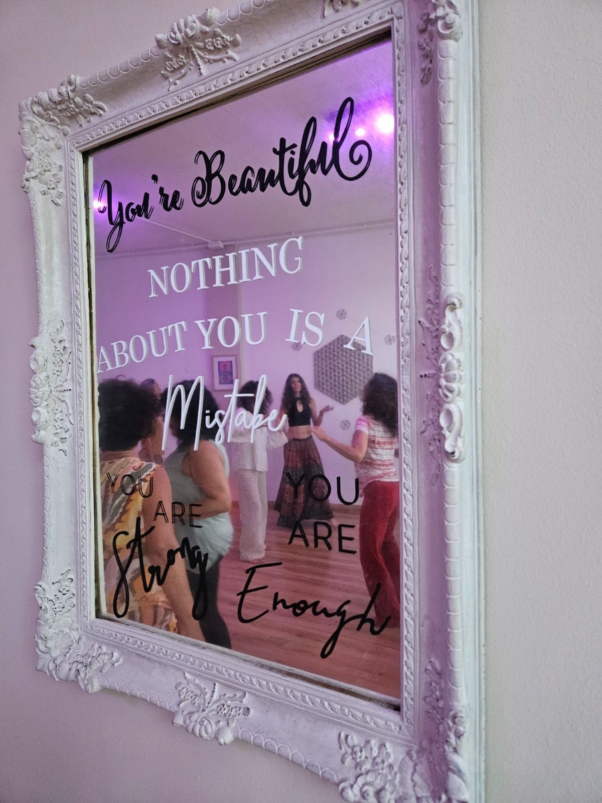 Espejo con marco blanco y texto inspirador que refleja una clase de baile. La gente baila en un estudio.