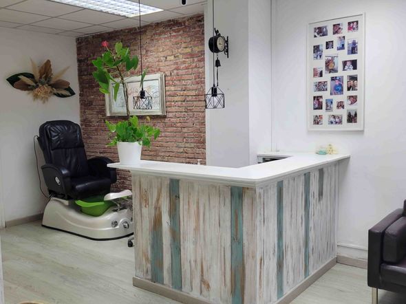 Área de recepción de un salón de uñas con un mostrador de recepción de madera rústica y una silla de pedicura en la esquina.