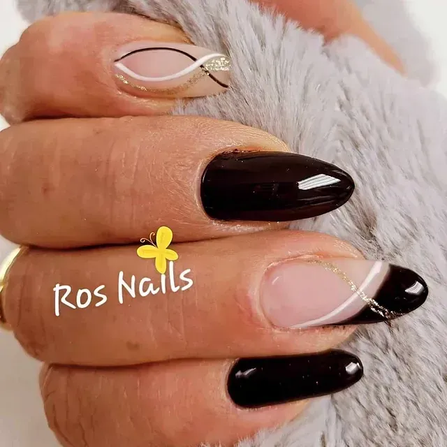 Primer plano de una mano con uñas almendradas. La mayoría son negras, una tiene un diseño de espirales blancas y doradas. La mano reposa sobre una superficie gris suave.