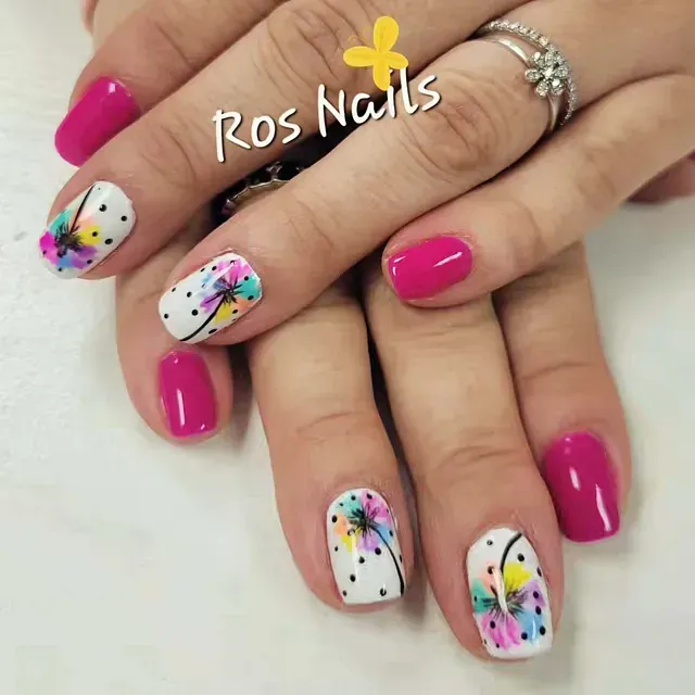Primer plano de las manos de una persona que muestra uñas de color magenta y uñas con base blanca, puntos negros y diseños de plumas de acuarela de colores.