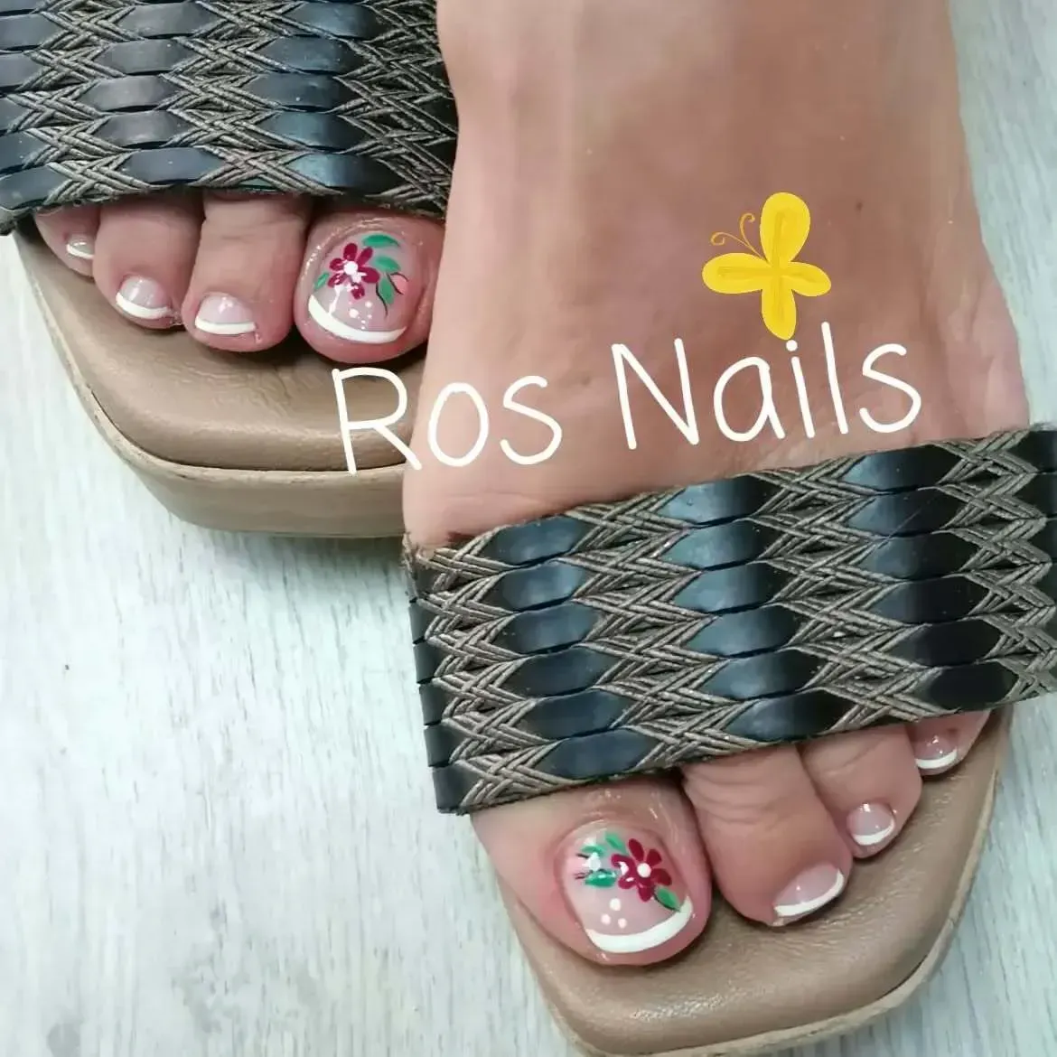 Pie con nail art floral y puntas francesas blancas en sandalias con tira trenzada; logo Ros Nails.