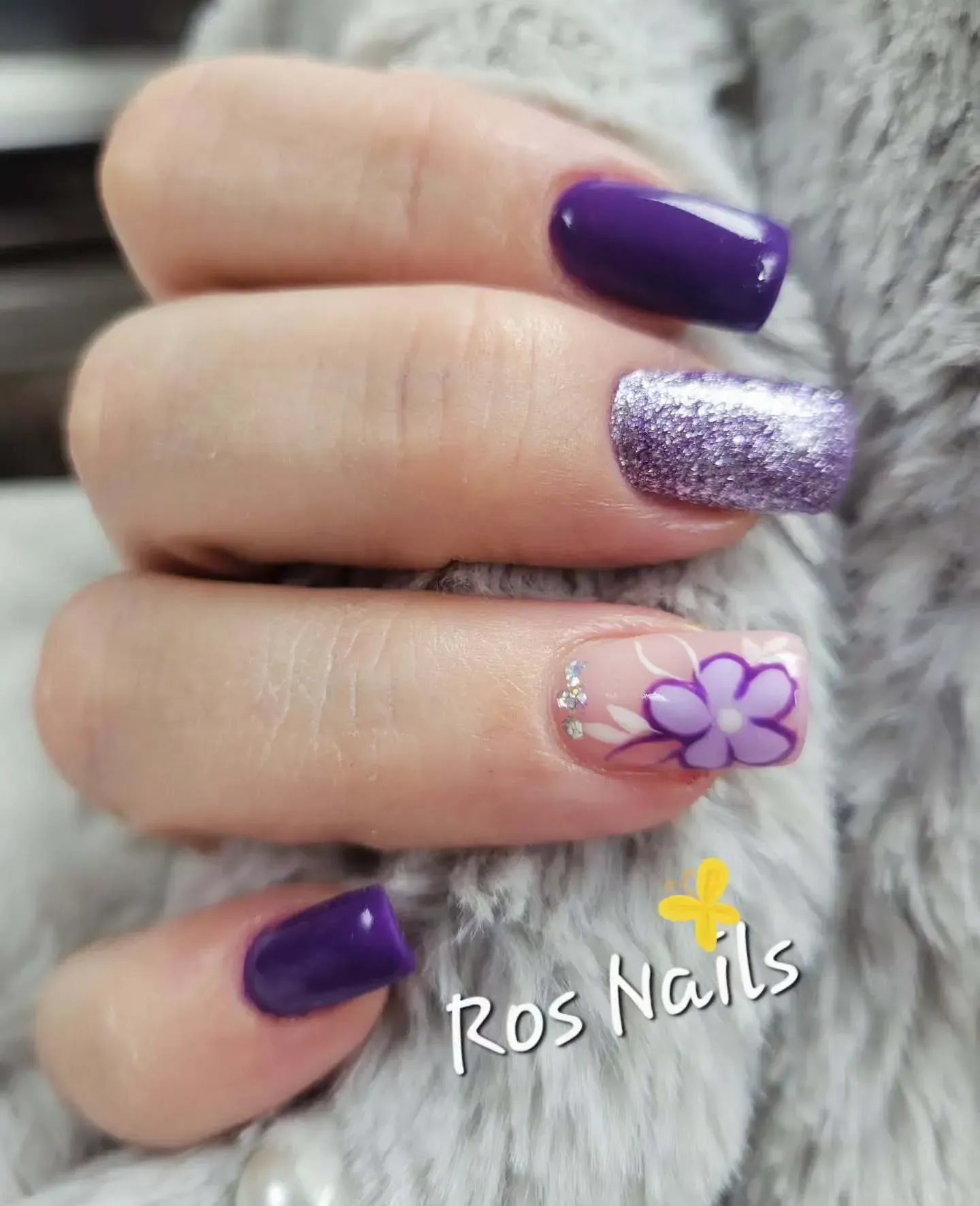 Pies en sandalias blancas con uñas color lavanda, una de ellas acentuada con un diseño de hojas negras.