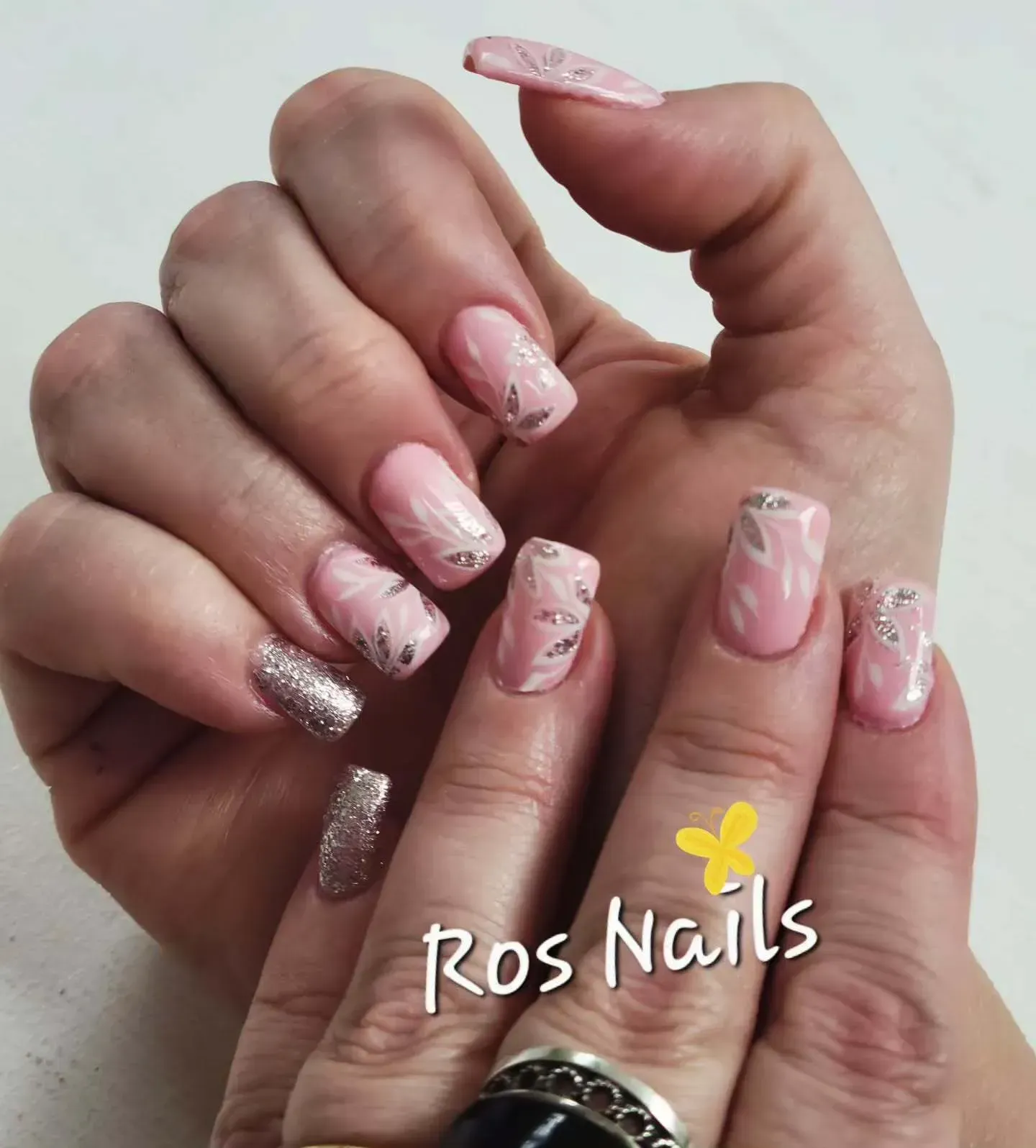 Pie con nail art floral y puntas francesas blancas en sandalias con tira trenzada; logo Ros Nails.