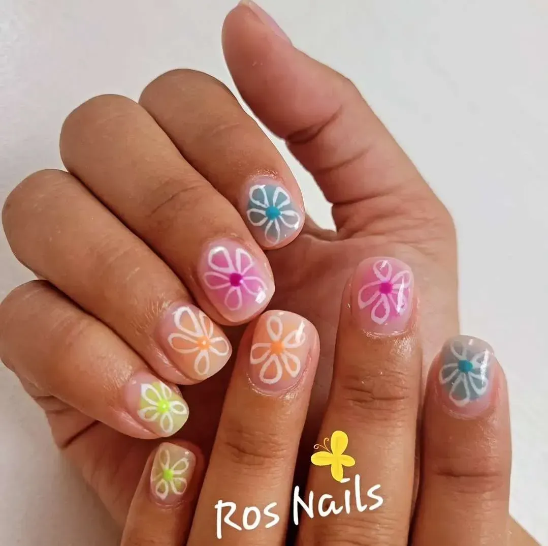 Pie con nail art floral y puntas francesas blancas en sandalias con tira trenzada; logo Ros Nails.