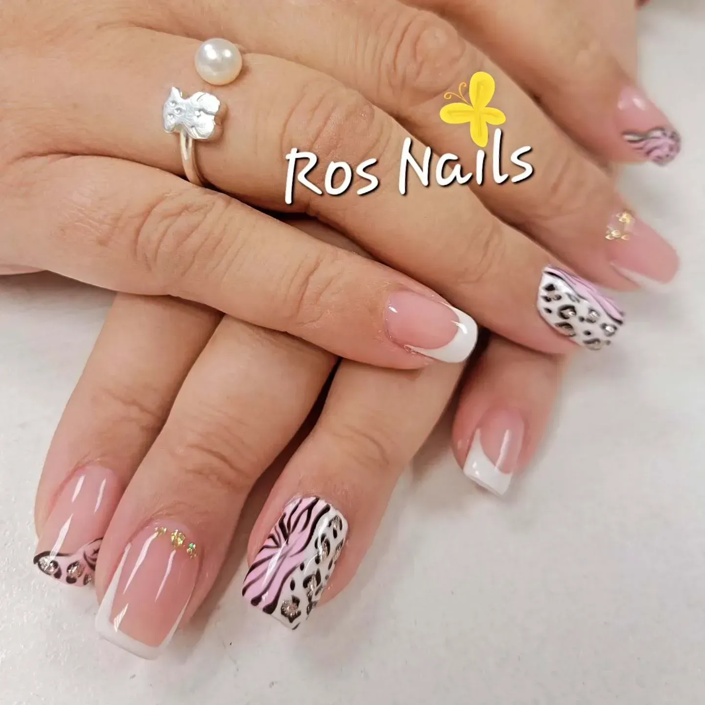 Par de pies con uñas de punta francesa, apoyados sobre una superficie texturizada, con una flor rosa.