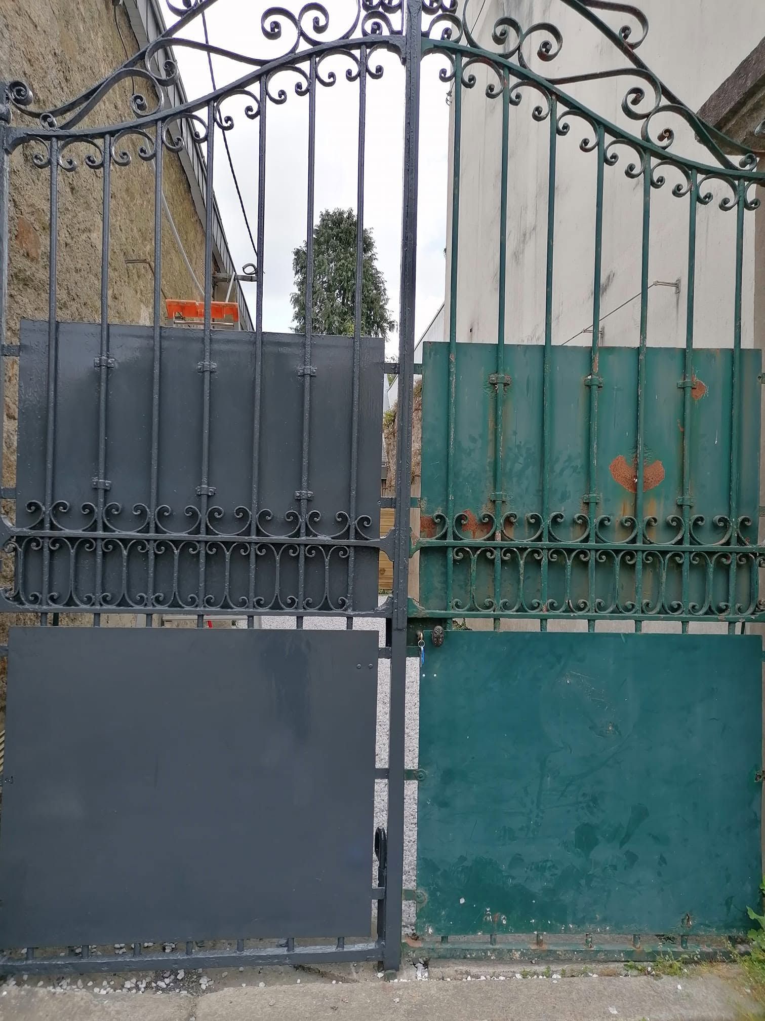 Portail métallique fermé à panneaux gris et verts devant la cour d'un immeuble.