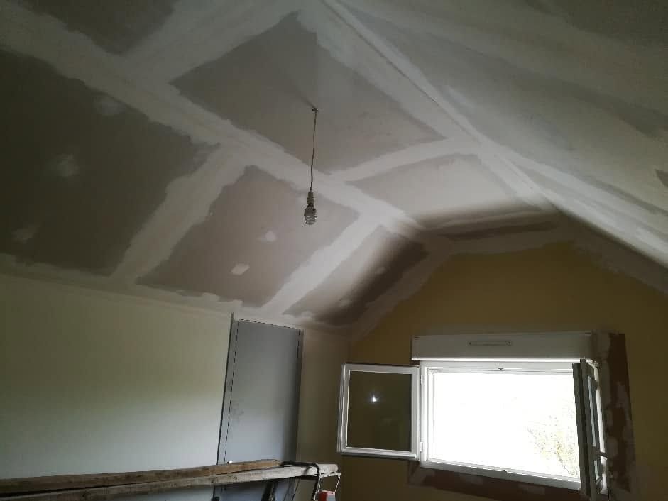 Pièce partiellement aménagée avec un plafond en plaques de plâtre jointoyées et une fenêtre ouverte.