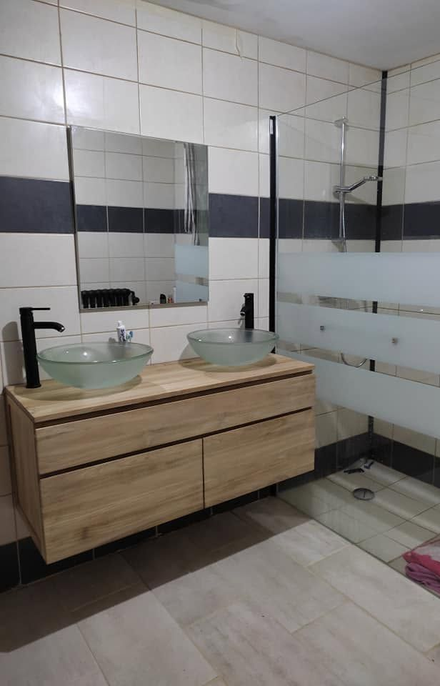 Salle de bains moderne avec double vasque en bois, lavabos en verre, miroirs et murs carrelés.
