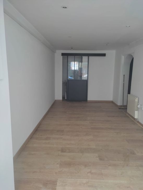 Pièce blanche vide avec parquet, porte grise au fond et spots encastrés au plafond.