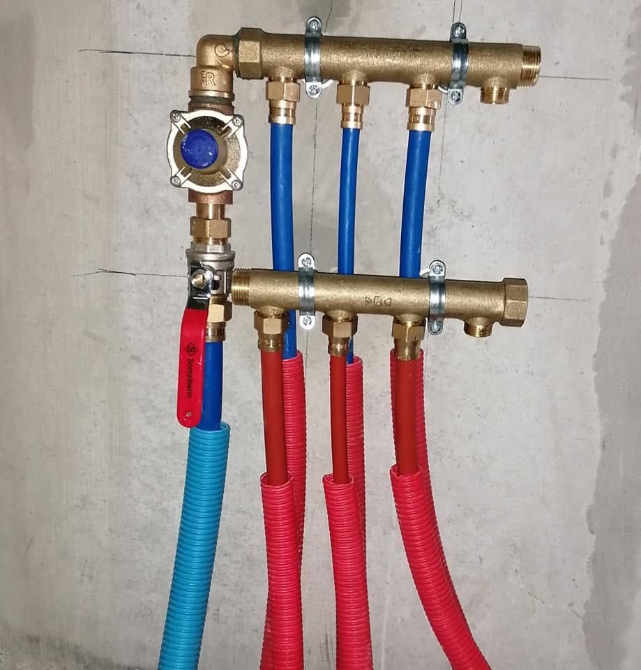 Collecteur de plomberie en laiton avec tuyaux bleus et rouges, monté sur un mur en béton.