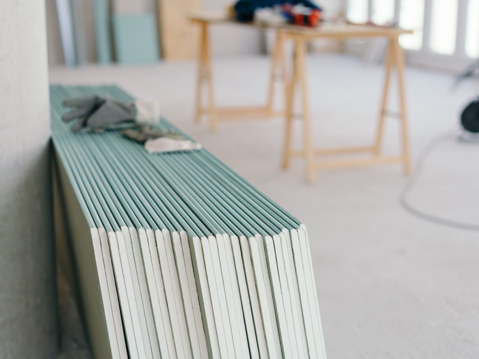 Des plaques de plâtre, appuyés contre un mur dans une pièce avec des tables en bois en arrière-plan.