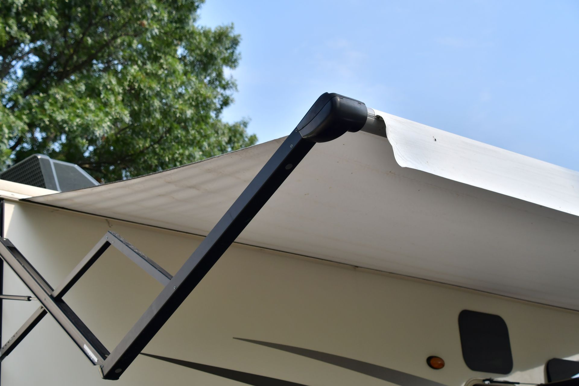 Auvent de camping-car déployé au-dessus d'une caravane, avec des bras de support noirs se détachant sur un ciel bleu.