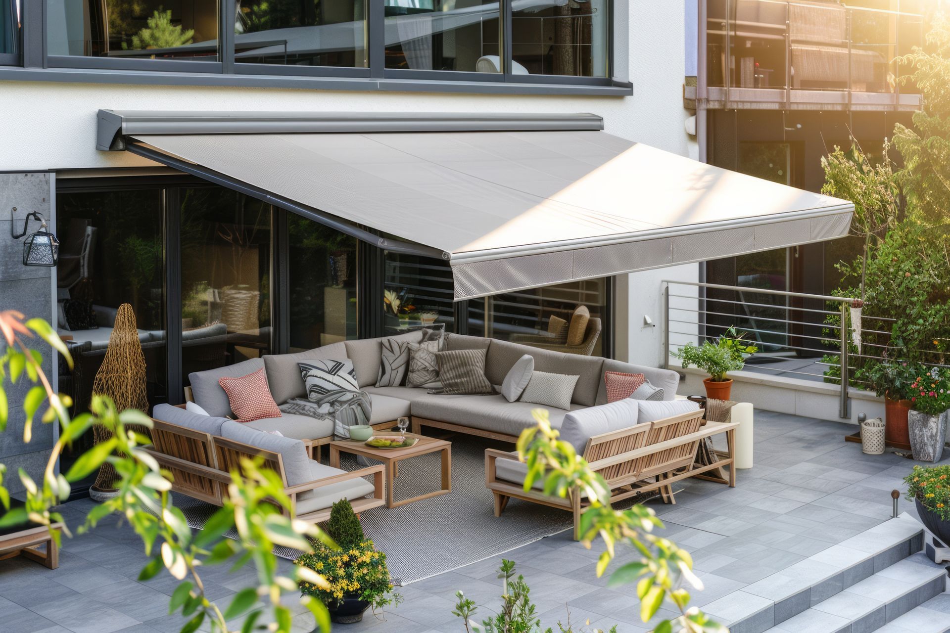 Terrasse moderne avec canapés en osier, un grand auvent beige et des plantes en pot devant une maison contemporaine.