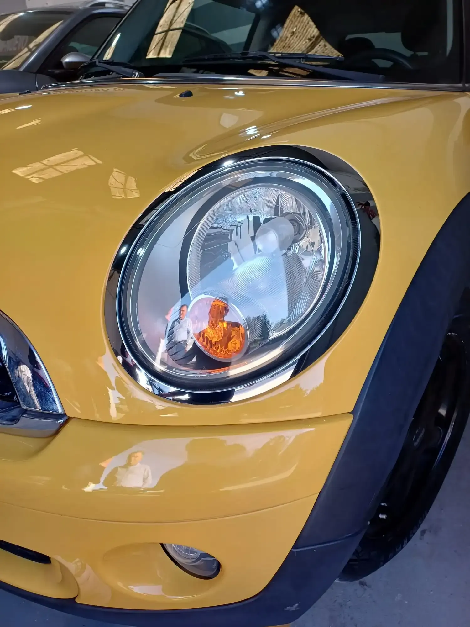 Primer plano del faro delantero y el parachoques de un Mini Cooper amarillo.
