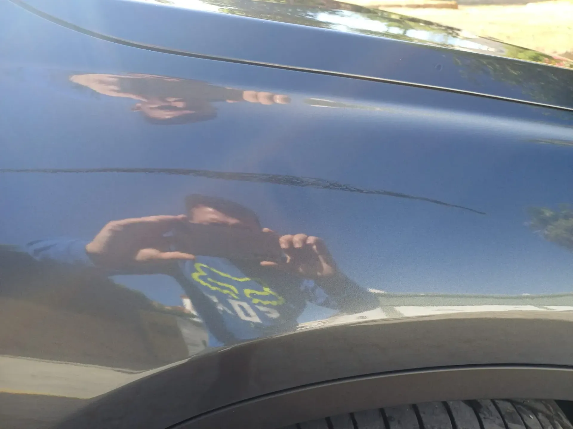 Reflejo de una persona tomando una fotografía en la puerta azul brillante de un coche.