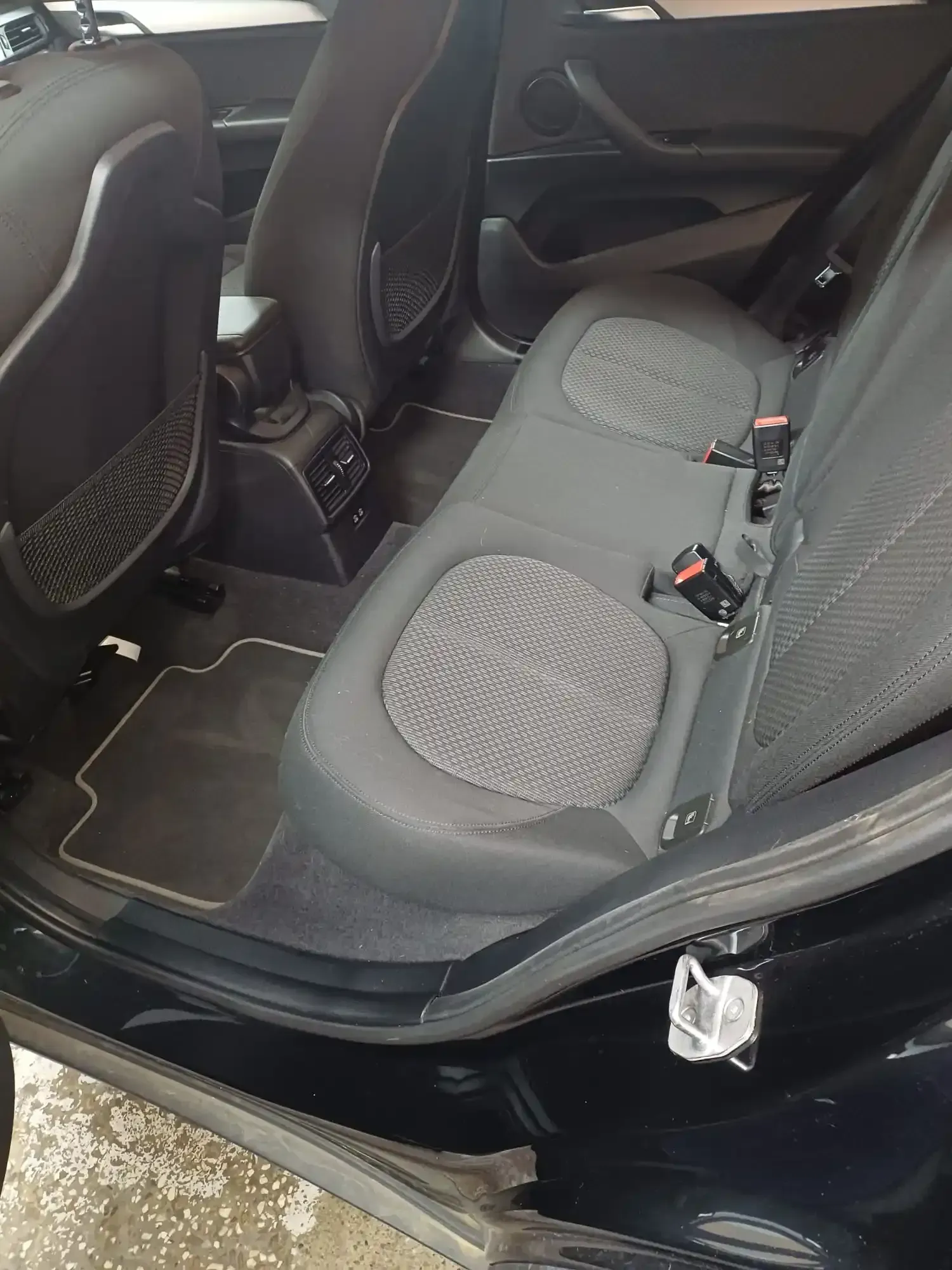 Asiento trasero para coche con tapicería de tela gris y alfombrillas en un interior de vehículo negro.