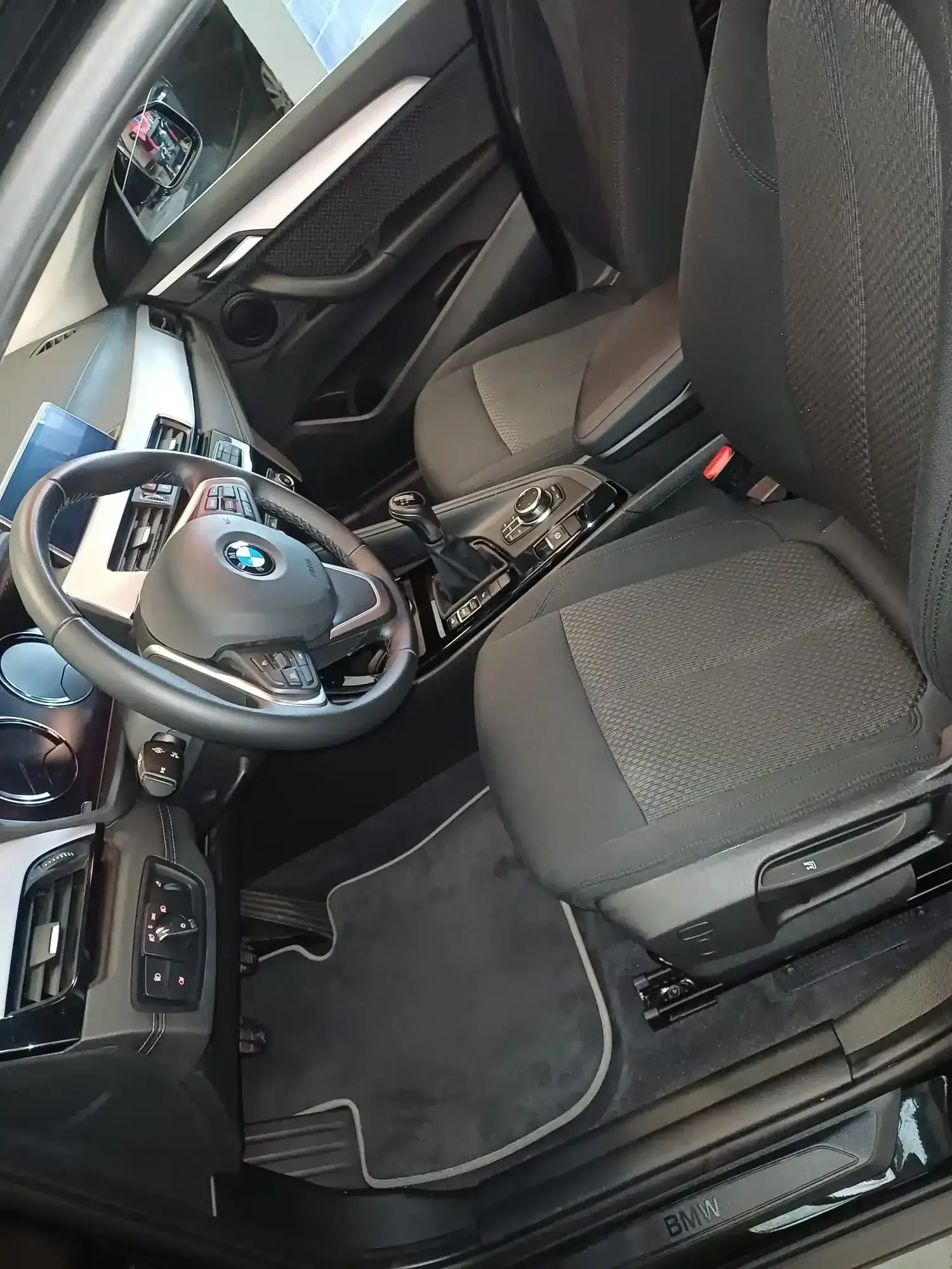 Interior de un automóvil BMW con volante, asiento delantero y consola central, visto desde el lado del conductor.