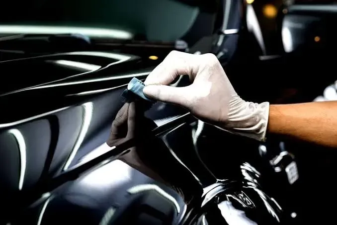 Una mano enguantada pule la puerta de un coche negro brillante con un paño azul.