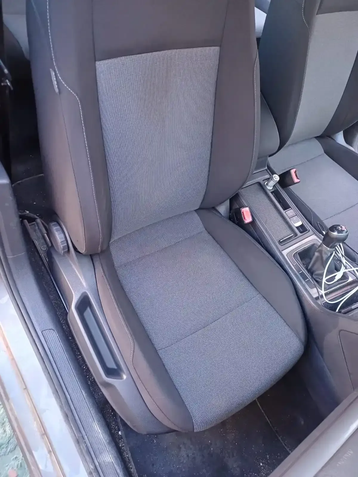 Asiento del pasajero delantero con tapicería gris y refuerzos laterales negros, situado junto a una consola central.