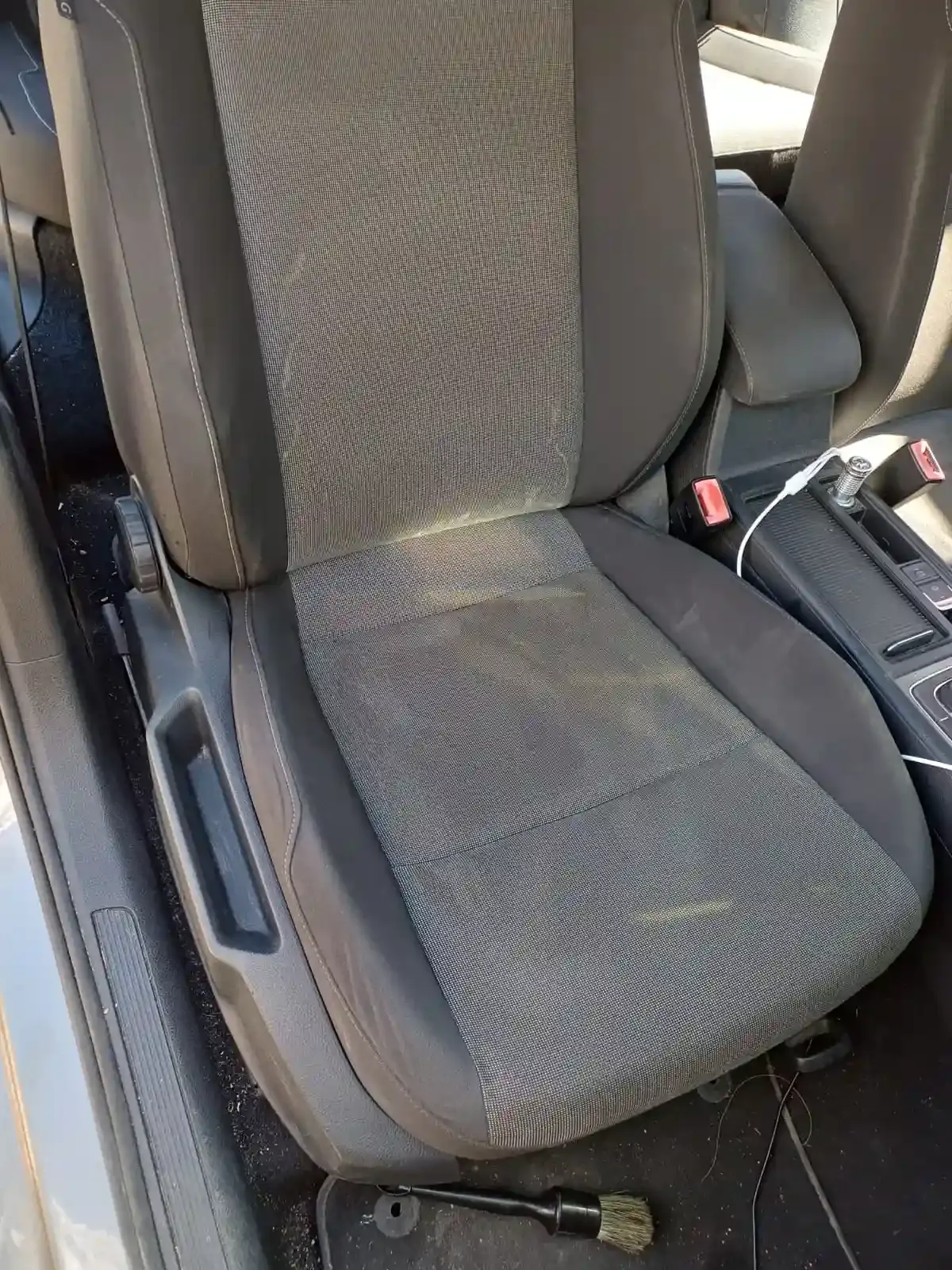 Cojín para asiento de coche con asiento de tela gris y controles laterales, visto desde el interior de un vehículo.