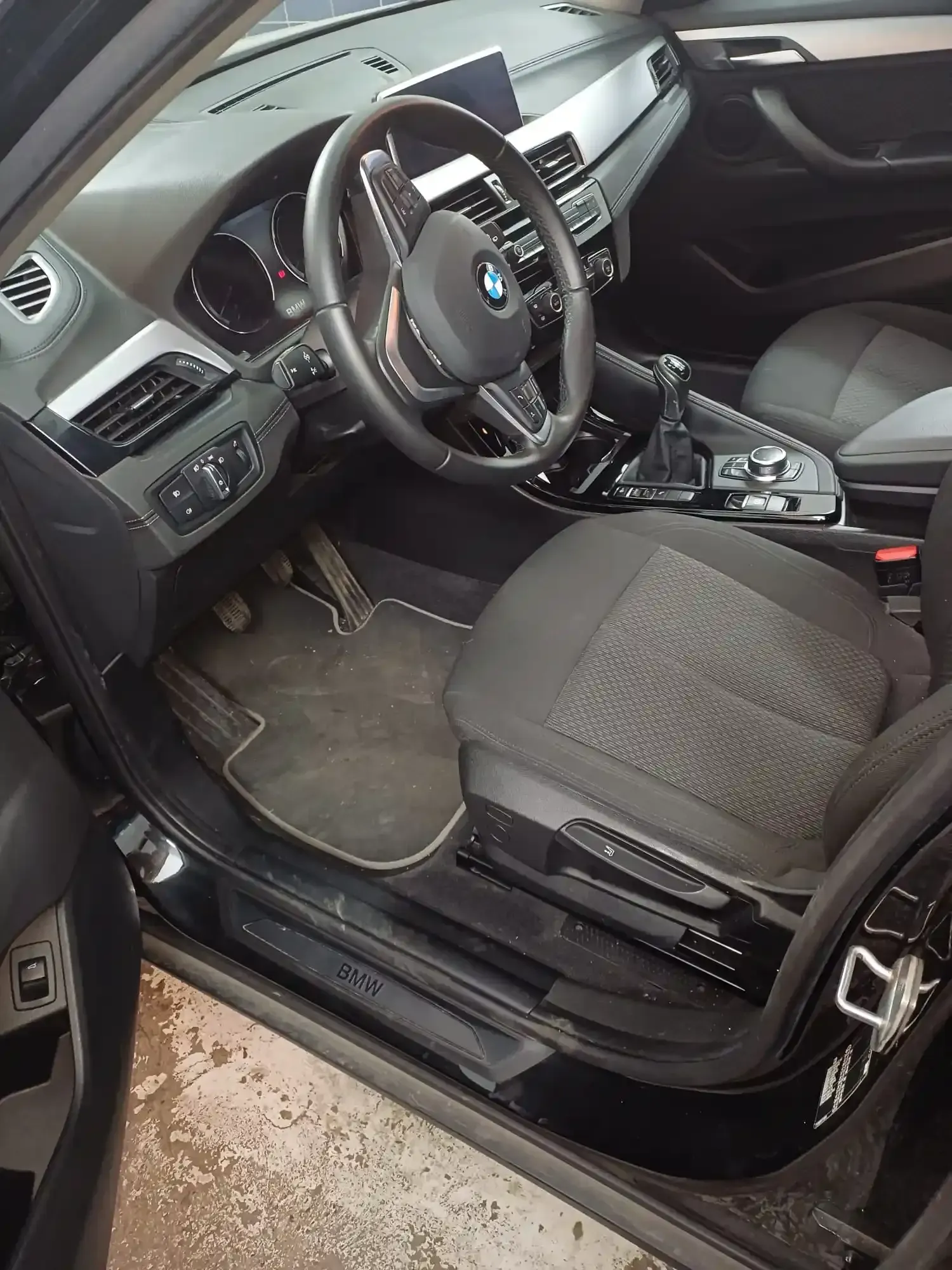 Interior del coche con asientos, volante y consola central negros, visto desde la puerta del conductor abierta.