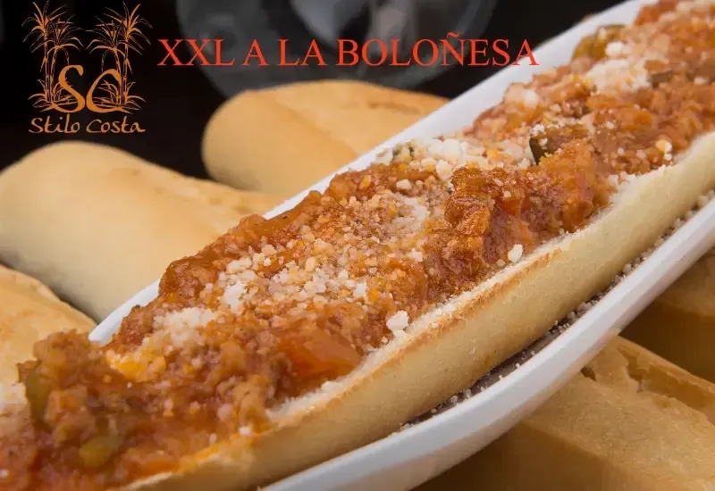 Bandeja de espaguetis a la boloñesa cubiertos con queso rallado, con pan al fondo.