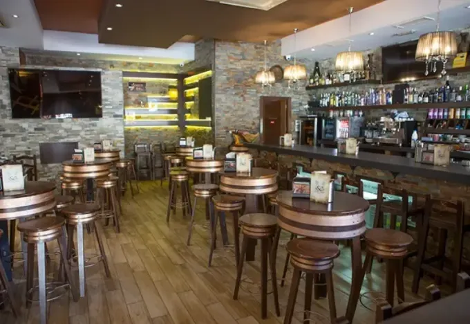 Interior de bar moderno y vacío con taburetes de madera, mesas y estantes con botellas detrás de la barra.