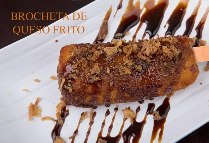Brocheta de queso frito en un plato blanco con sirope de chocolate y migas