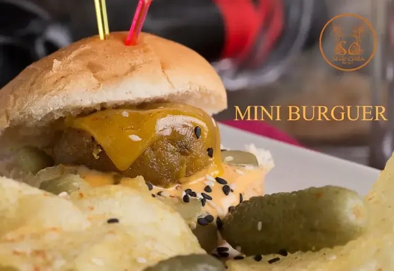 Mini hamburguesa con queso fundido y pepinillos en un plato, etiquetado como “MINI HAMBURGUESA”.