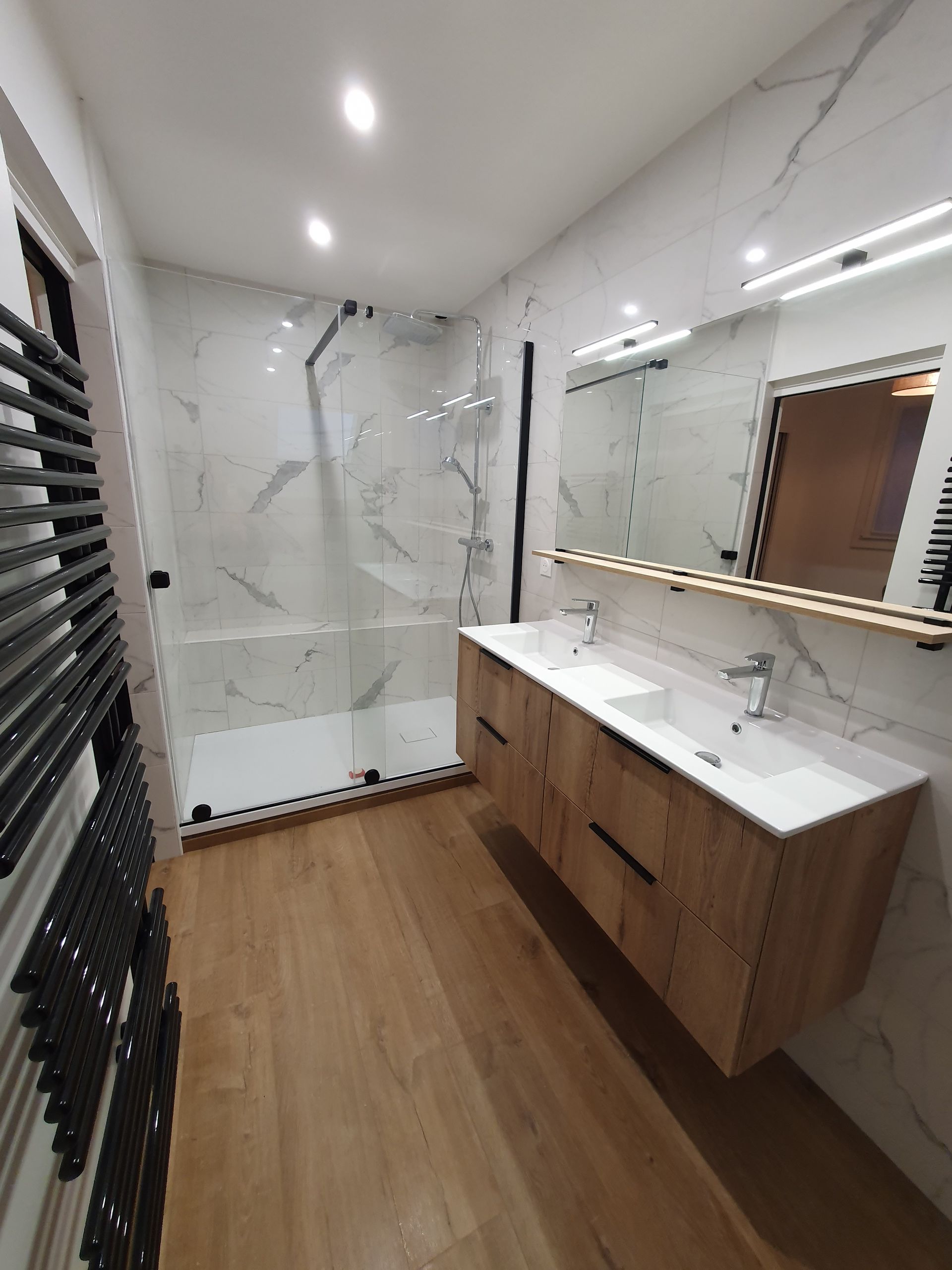 Salle de bains moderne et accessible avec deux lavabos, miroirs ovales, mur d'accent noir et baignoire blanche.
