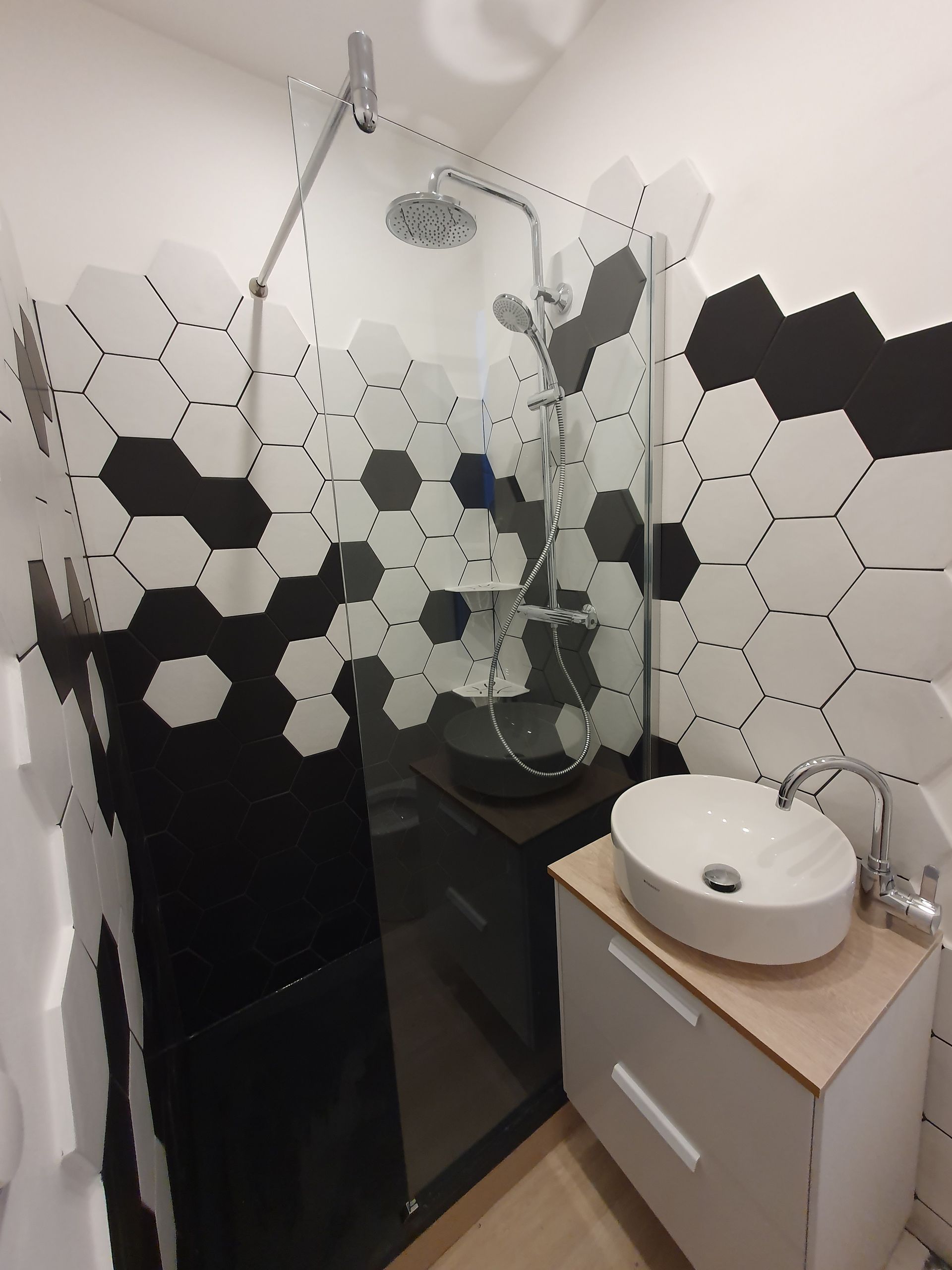 Salle de bains moderne avec douche carrelée de carreaux hexagonaux, paroi de douche en verre et meuble lavabo blanc.