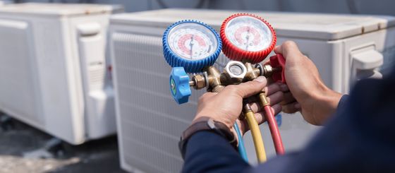 Des mains tenant des manomètres et des tuyaux de climatisation à côté d'unités de climatisation extérieures.