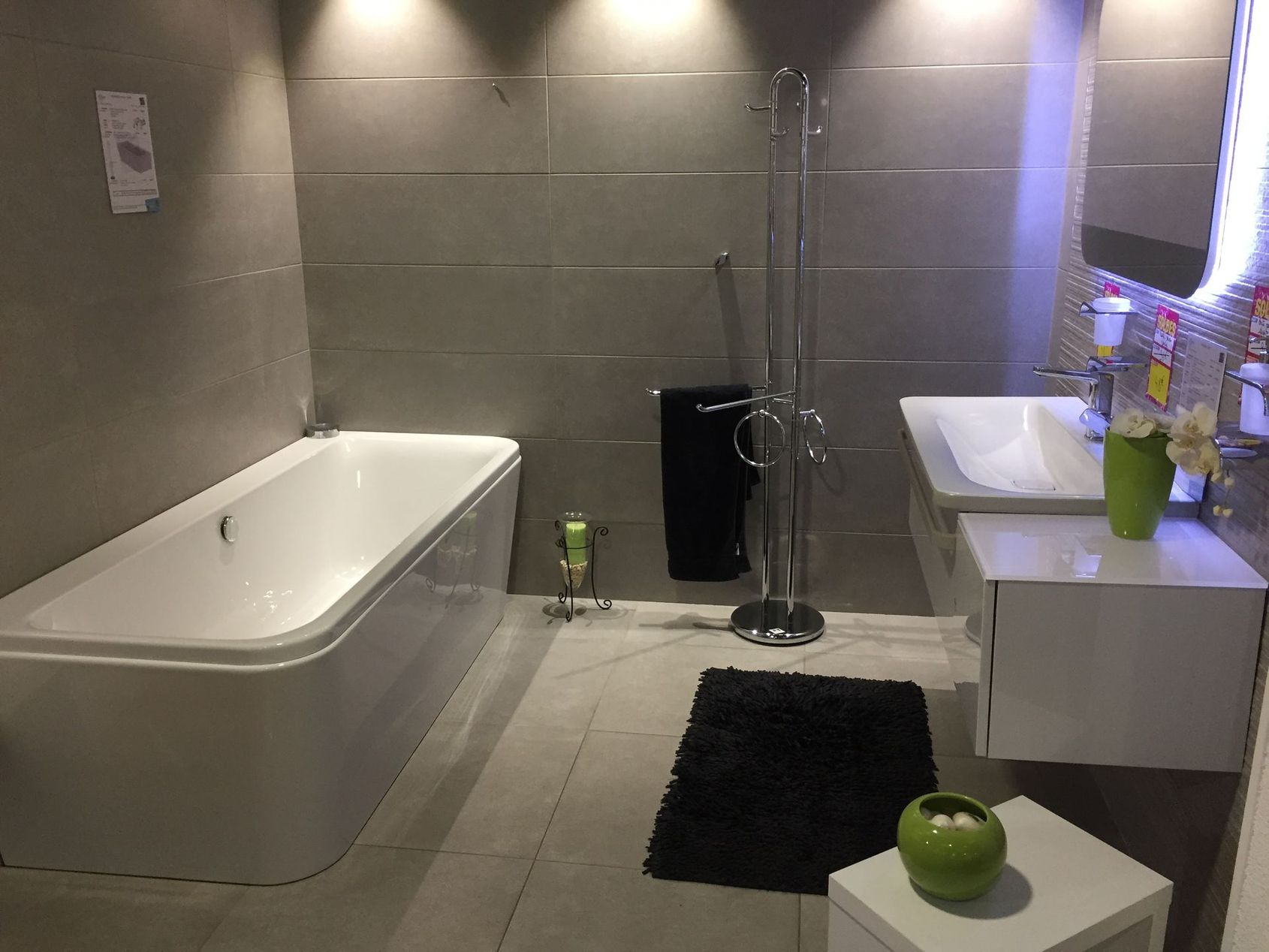 Salle de bains moderne avec baignoire et vasque blanches, tapis noir.