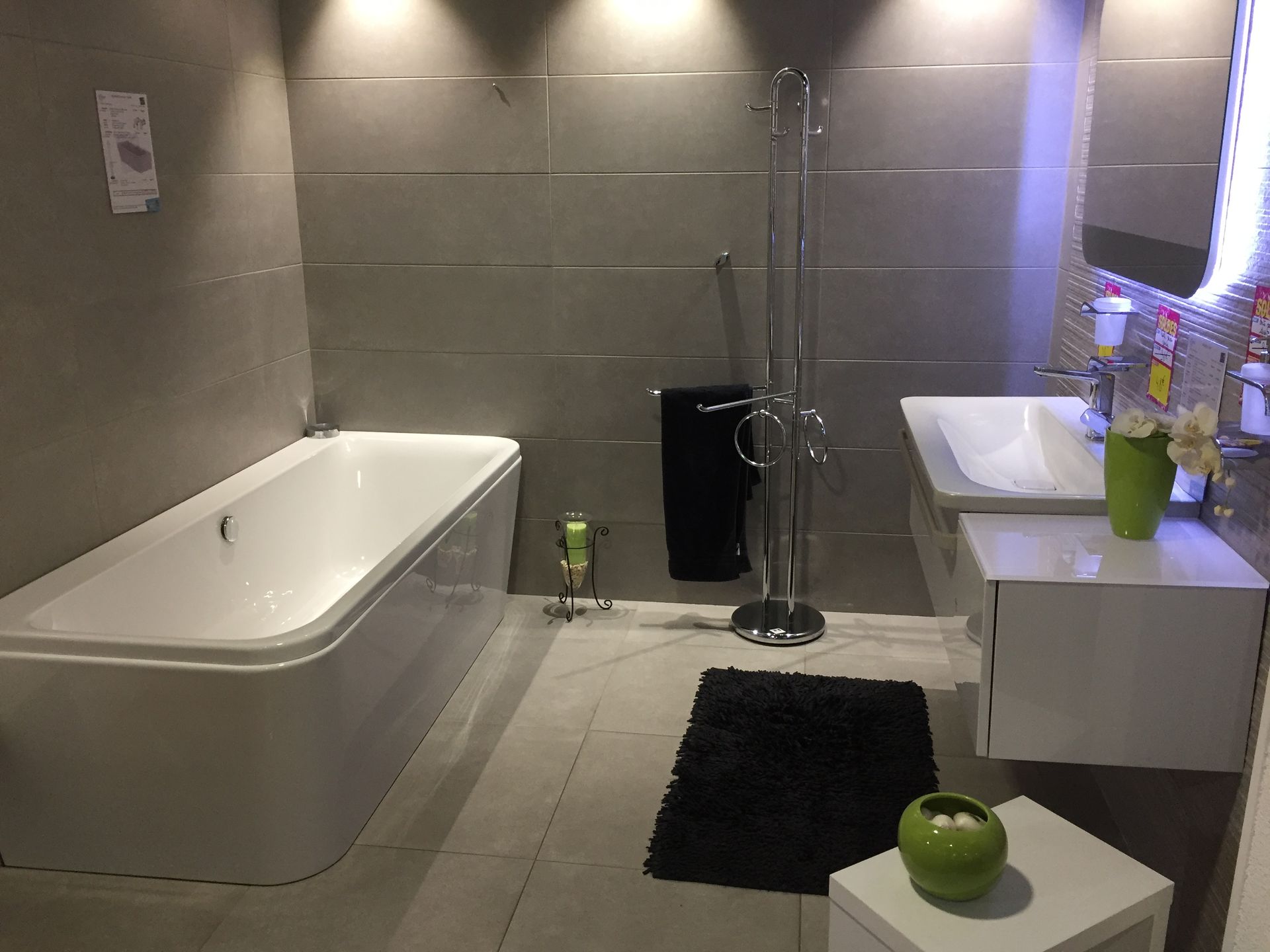 Salle de bains moderne avec baignoire et vasque blanches, tapis noir.