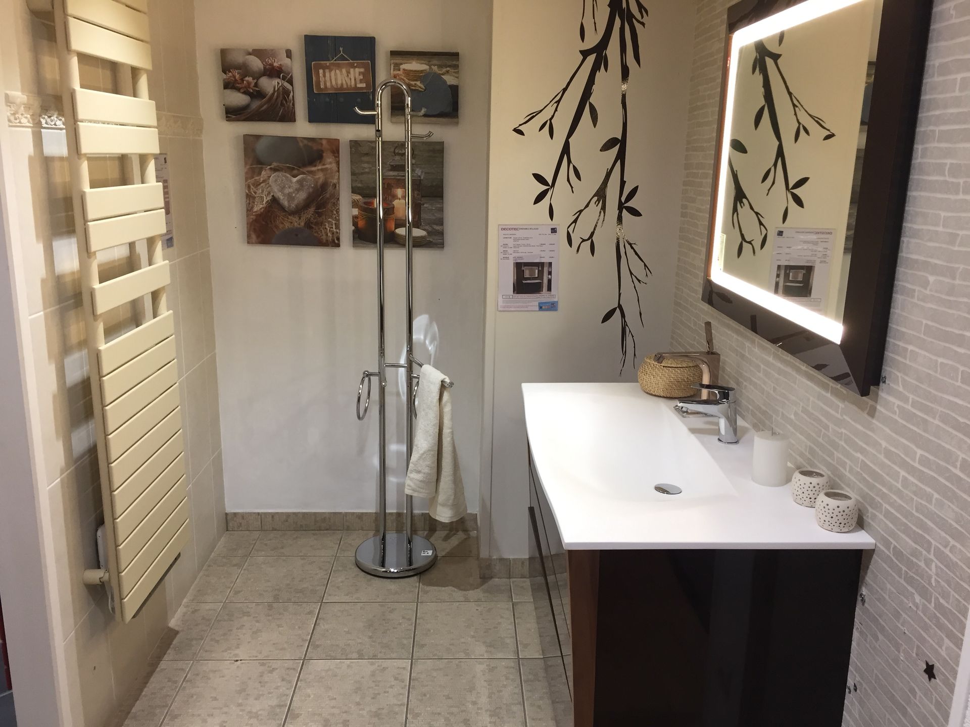 Salle de bains moderne avec vasque blanche, miroir, décoration murale et branches décoratives.
