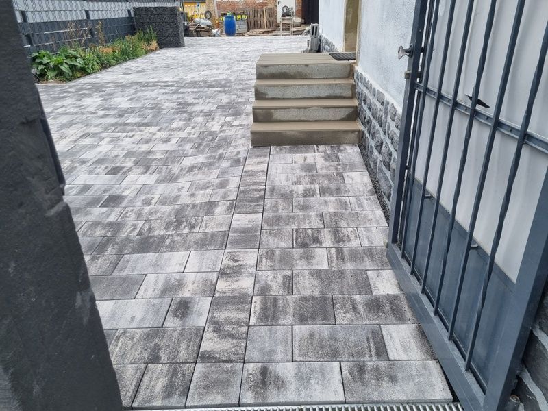 Über eine Ziegelsteintreppe gelangt man zu einer dunklen Steinstützmauer in einem Hinterhof mit einer Terrasse aus roten Ziegelsteinen.